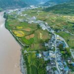 Aerial view of lush terraced rice fields along a winding river in a rural village, showcasing sustainable agriculture practices and scenic landscape at Sustax.