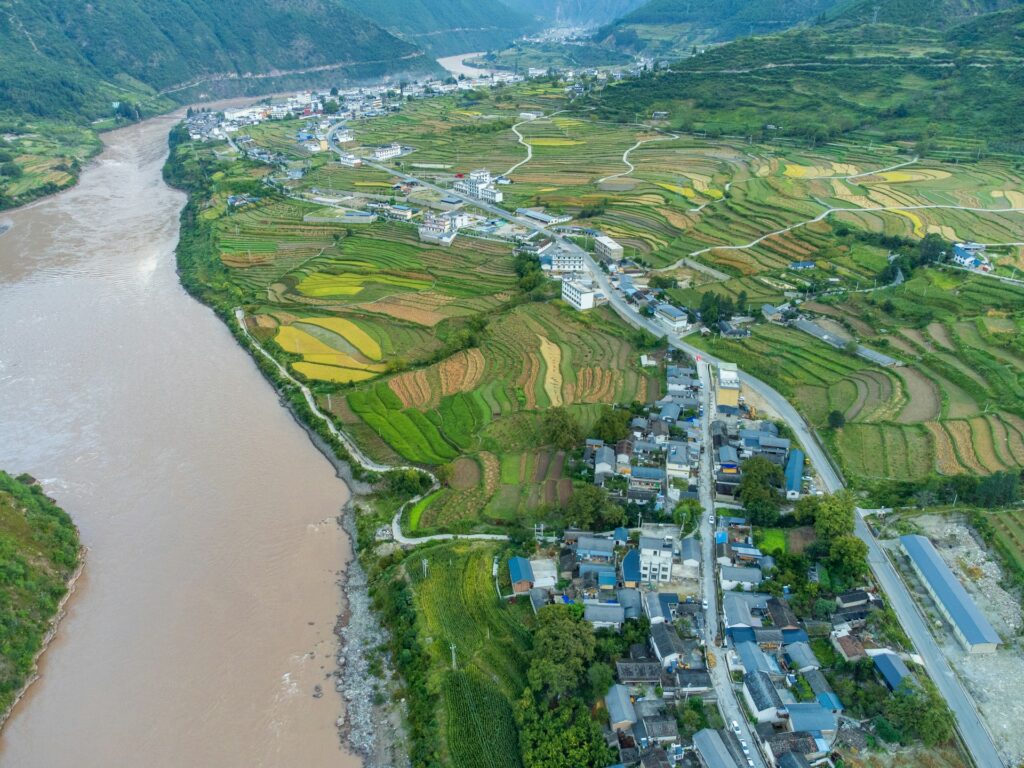 Aerial view of lush terraced rice fields along a winding river in a rural village, showcasing sustainable agriculture practices and scenic landscape at Sustax.